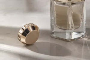 A premium studio close-up showing a custom metal perfume cap alongside a glass bottle, emphasizing finish quality and hand feel.